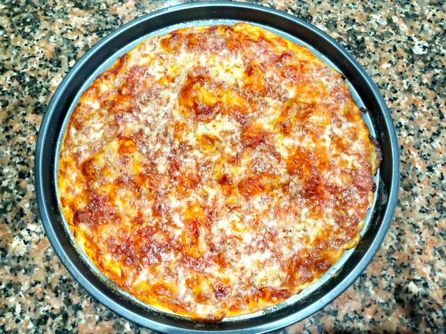 Pizza entera horneada en su bandeja sobre granito, con el queso dorado y el borde tostado