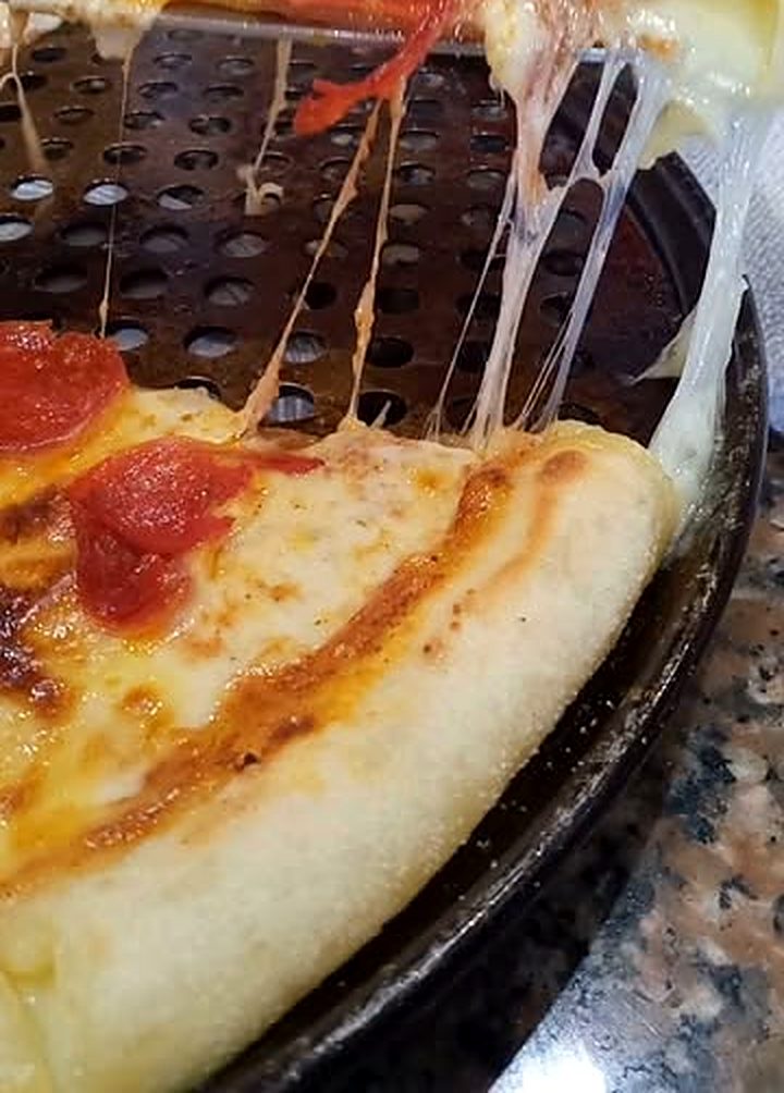 Una porción de Pizzalvi levantada de la bandeja, con hilos de queso mozzarella derretido que se estiran hacia la pizza